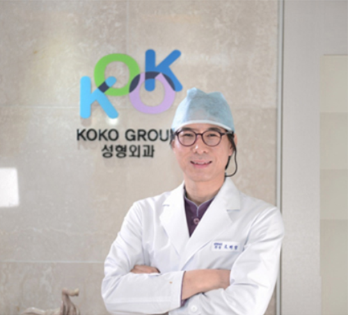 KOKO美容外科の院長ジョ・ベジョン院長がKOKO美容外科のロゴの前で腕を組んで立っている写真