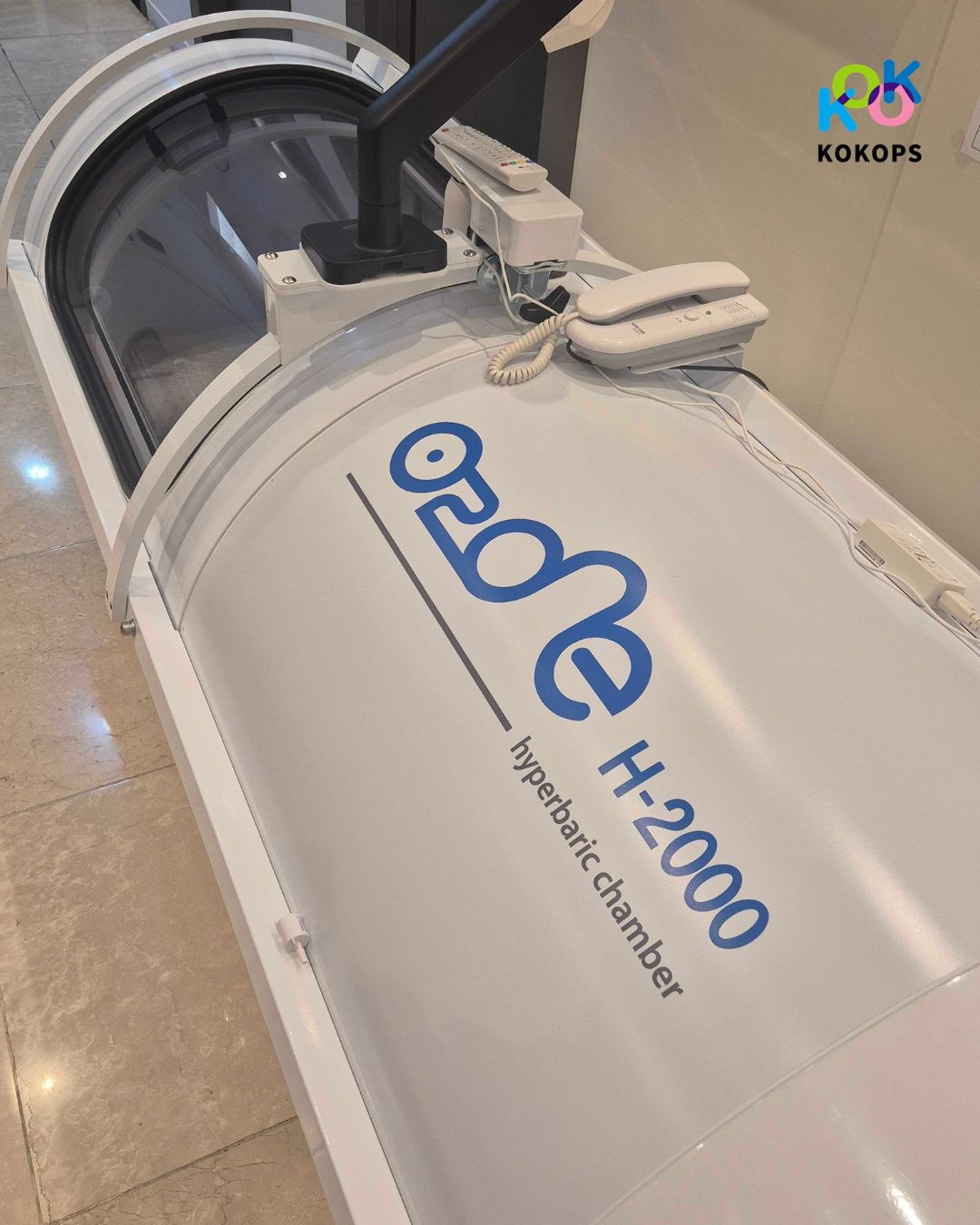 韓国の鼻整形の名医を選ぼう+高圧酸素治療装置 導入 2 | Korea's Top Nose Revision Specialist 高圧酸素治療装置「O2 One H-2000」の本体上部のアップ写真。装置の上にはモニター用のアームや、外部と連絡をとるための白い電話機(インターホン)が設置されている。